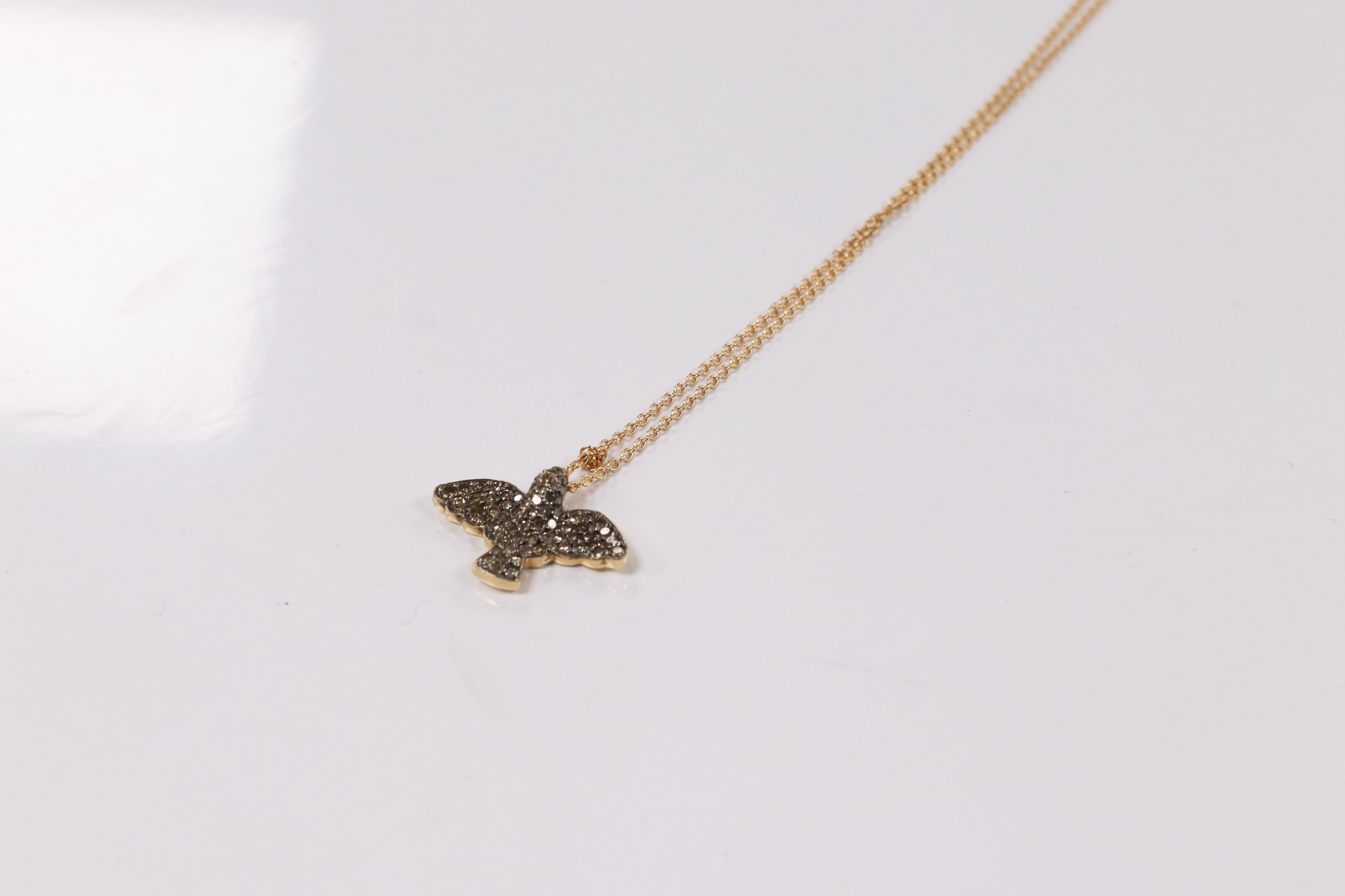 A modern 18k and pave set two colour diamond chip bird pendant, wing span 19mm, on an Italian 18k fine link chain, 36cm, gross weight 4.4 grams. Condition - fair to good